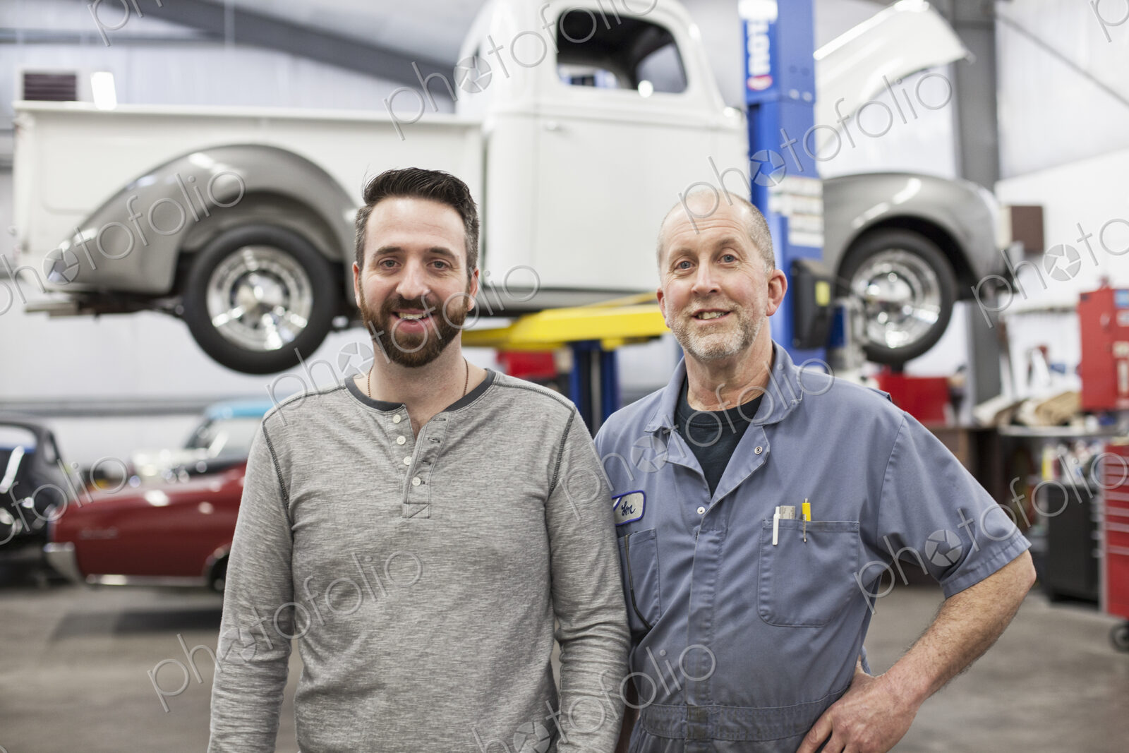 A portrait of a caucasian senior car mechanic and his son in their classic car repair…