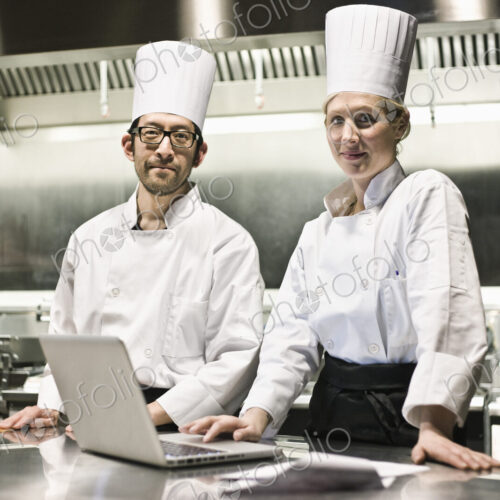 A portrait of a mixed race pair of chefs working with a laptop computer in a… A portrait of a mixed race pair of chefs working with a laptop computer in a…