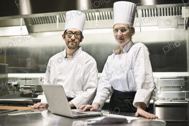 A portrait of a mixed race pair of chefs working with a laptop computer in a…