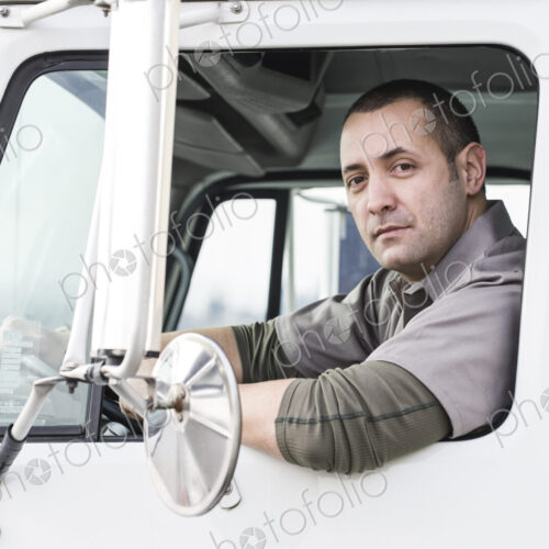A portrait of a uniformed male truck driver in the window of his truck at a… A portrait of a uniformed male truck driver in the window of his truck at a…