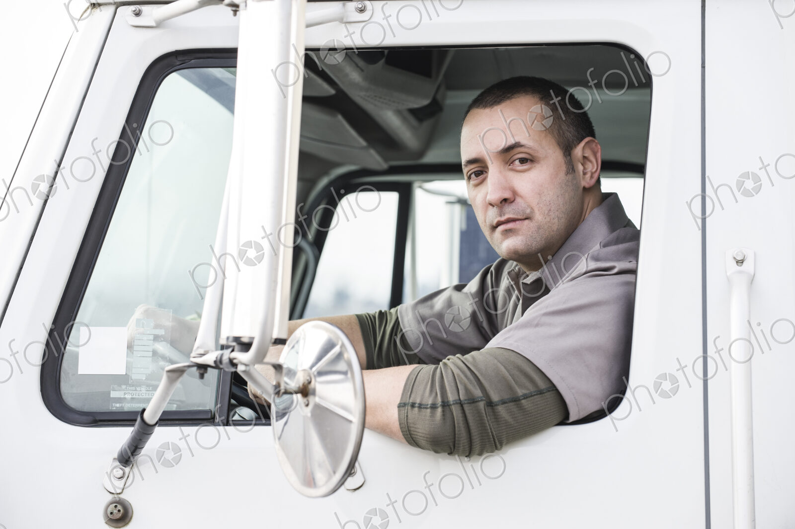 A portrait of a uniformed male truck driver in the window of his truck at a…