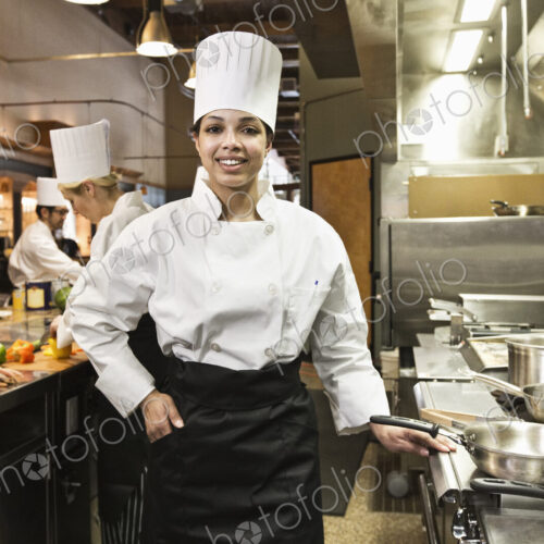A portrait of a young black female chef in a commercial kitchen with her crew working… A portrait of a young black female chef in a commercial kitchen with her crew working…