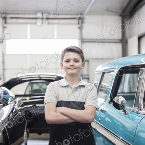 A portrait of a young caucasian boy in his father's classic car repair shop.