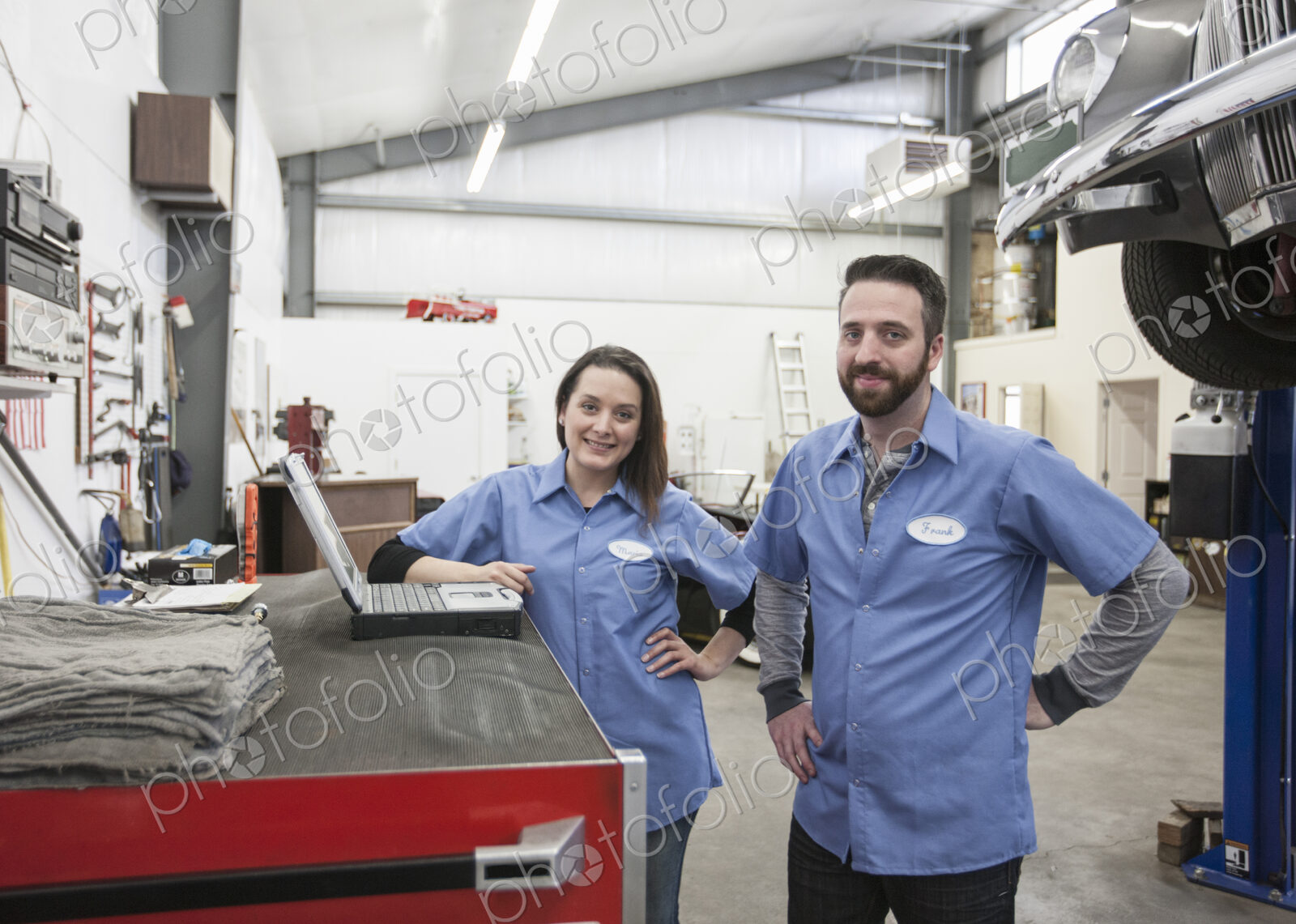 A portrait of two caucasian male and female mechanics in an antique car repair shop.