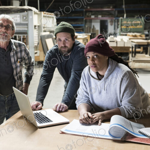 A portrati of mixed race carpenters around a laptop computer after work hours in a…