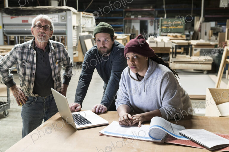A portrati of mixed race carpenters around a laptop computer after work hours in a…