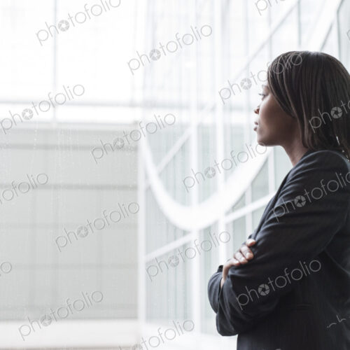 A portriat of a black businesswoman standing at a window in a convention center lobby.