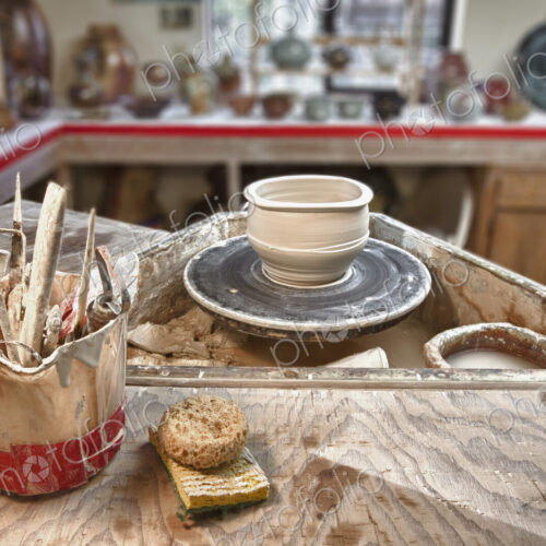 A potter's workshop, a potters wheel, working tools and sponges on a board, displays…
