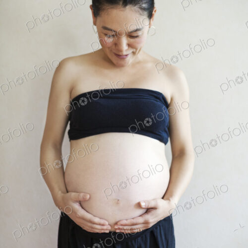 A pregnant woman holding her hands under the curve of her stomach, looking down. A pregnant woman holding her hands under the curve of her stomach, looking down.