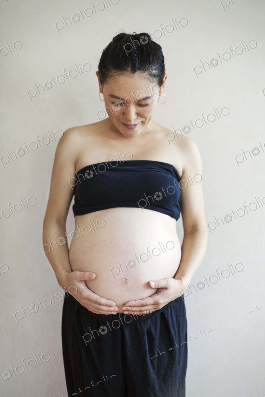 A pregnant woman holding her hands under the curve of her stomach, looking down.