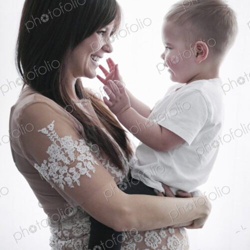 A pregnant woman holding her young son in her arms.