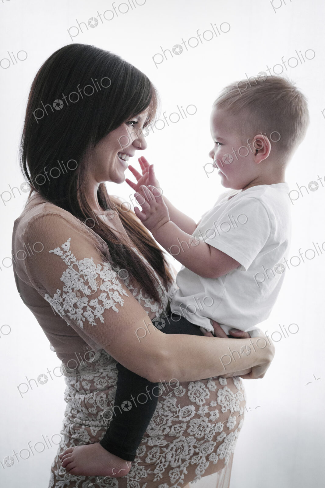 A pregnant woman holding her young son in her arms.