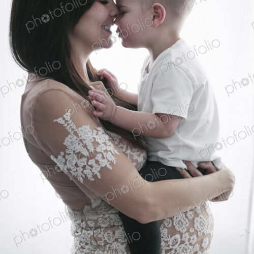 A pregnant woman holding her young son in her arms.