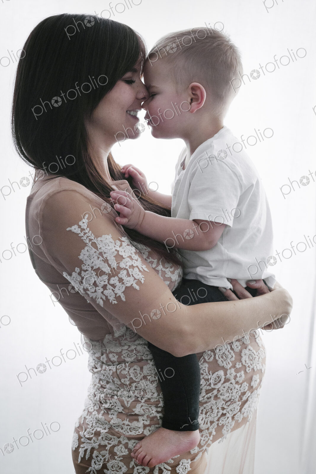 A pregnant woman holding her young son in her arms.