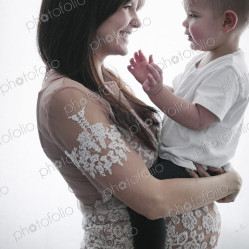A pregnant woman holding her young son in her arms.