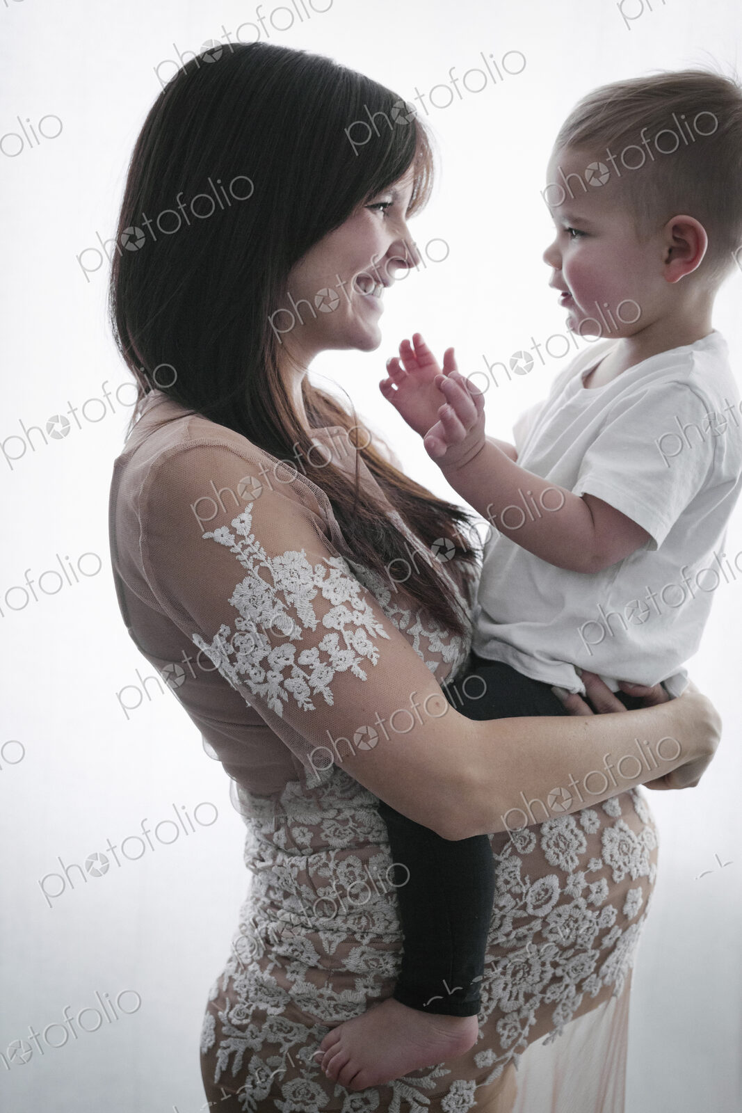 A pregnant woman holding her young son in her arms.