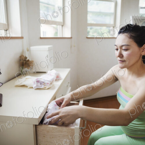 A pregnant woman in a baby's nursery room, folding baby clothes.