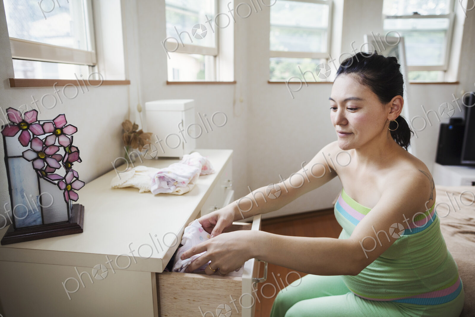 A pregnant woman in a baby’s nursery room, folding baby clothes.
