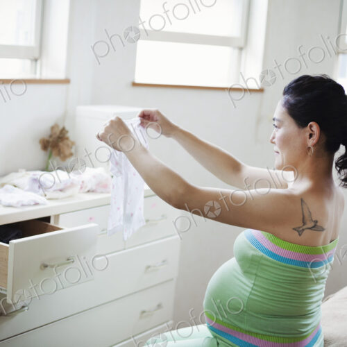 A pregnant woman in a baby's nursery room, folding baby clothes.