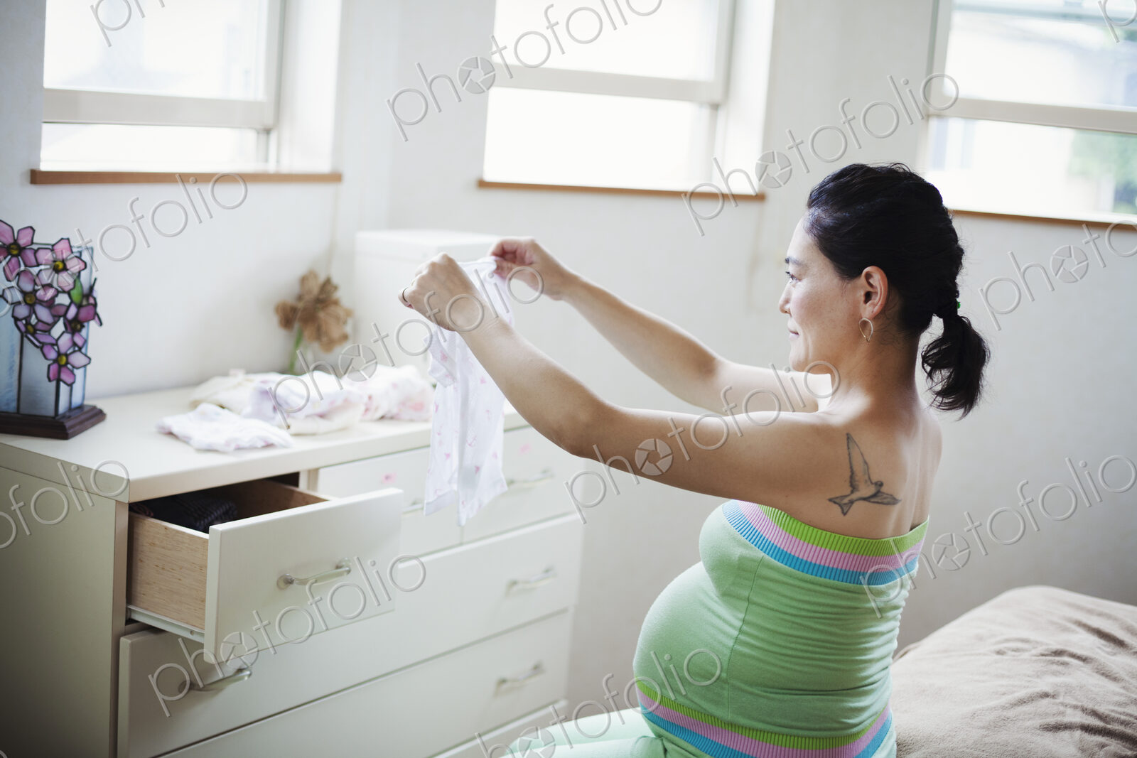 A pregnant woman in a baby’s nursery room, folding baby clothes.