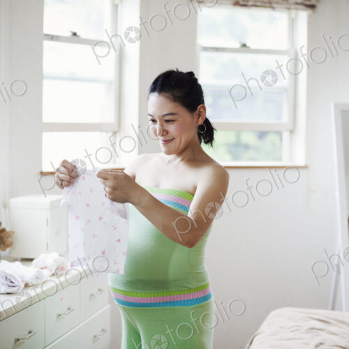 A pregnant woman in a baby's nursery room, folding baby clothes.