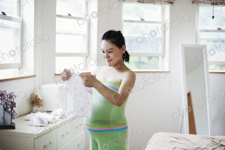 A pregnant woman in a baby's nursery room, folding baby clothes.