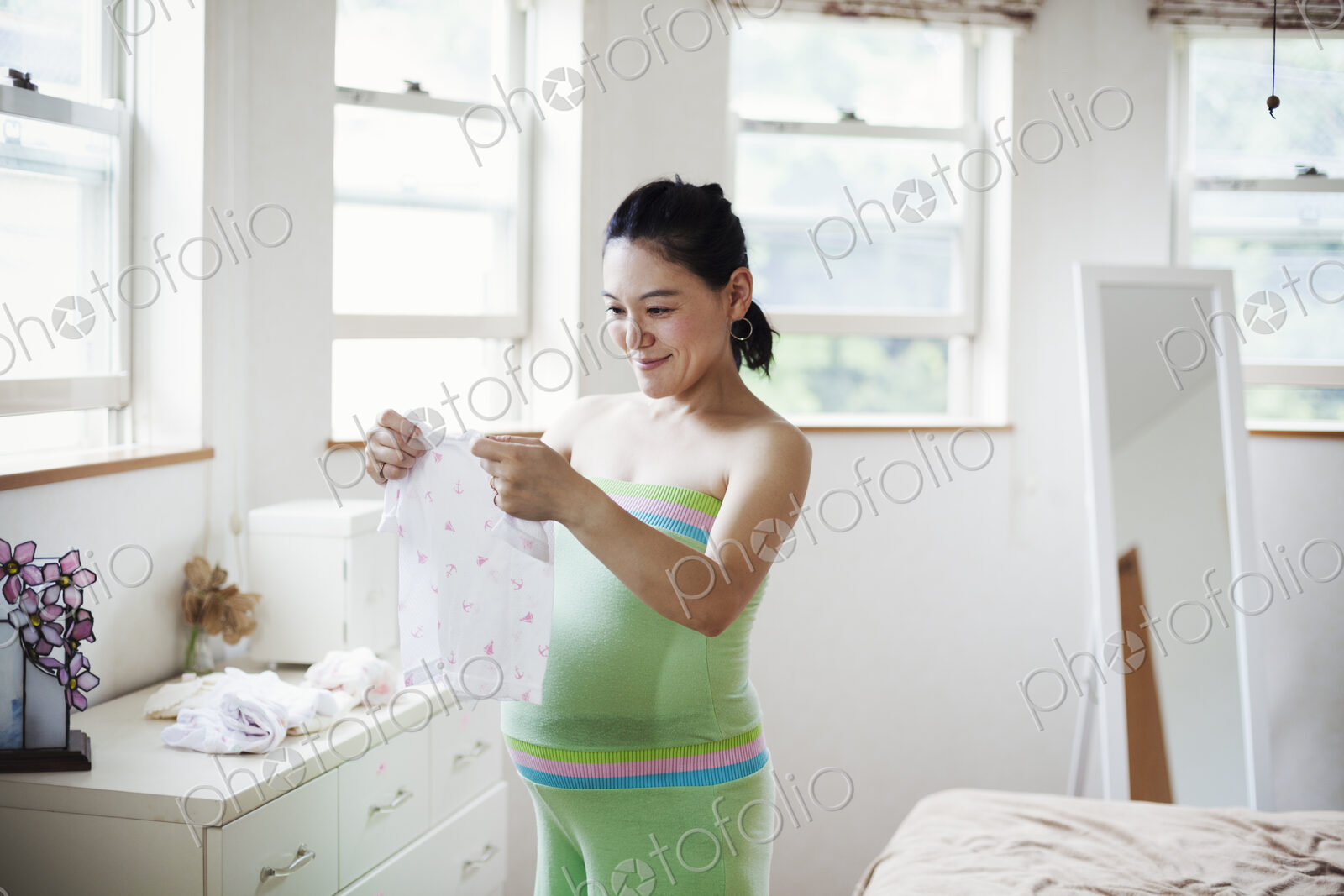 A pregnant woman in a baby’s nursery room, folding baby clothes.