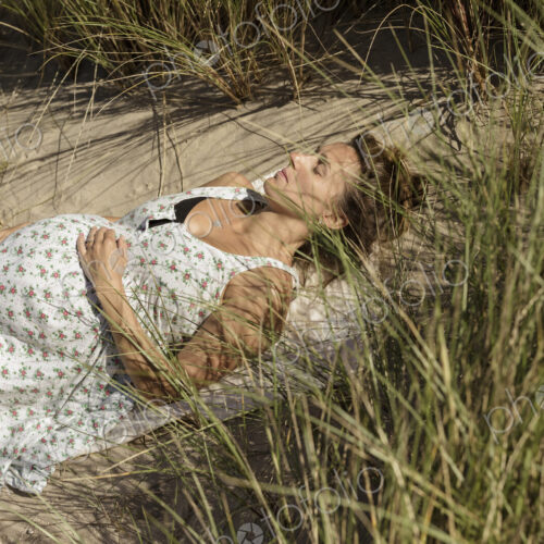 A pregnant woman lying in the sun in the sand dunes. Taking it easy.