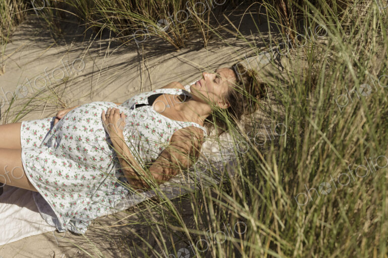 A pregnant woman lying in the sun in the sand dunes. Taking it easy.