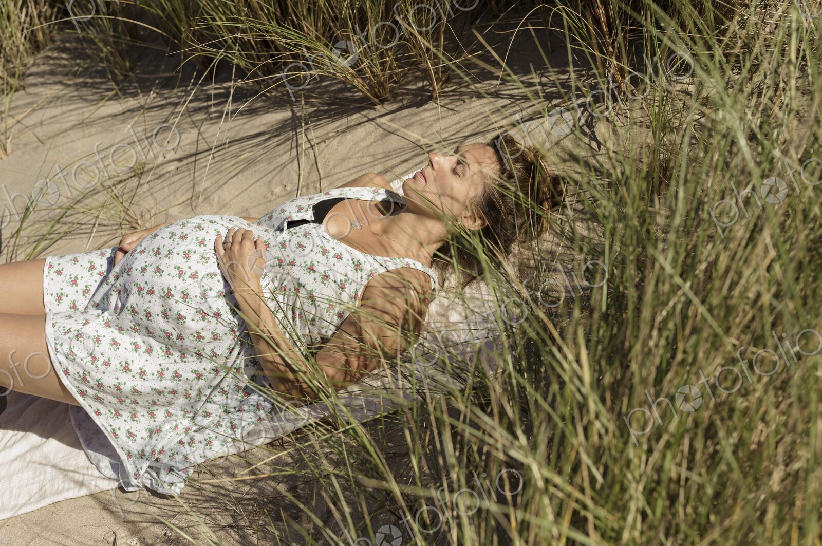 A pregnant woman lying in the sun in the sand dunes. Taking it easy.