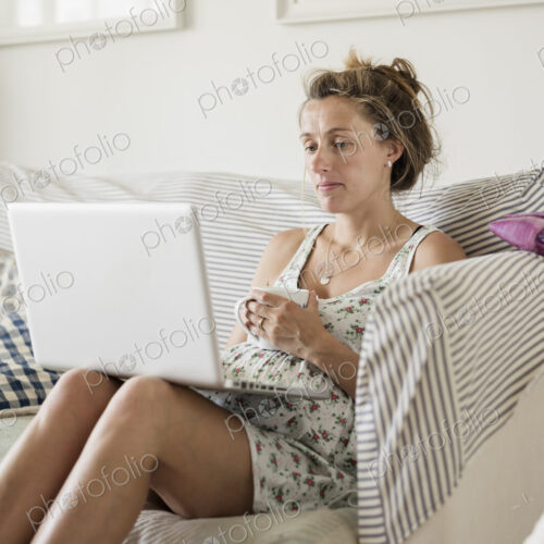 A pregnant woman seated on on a sofa with her feet up.