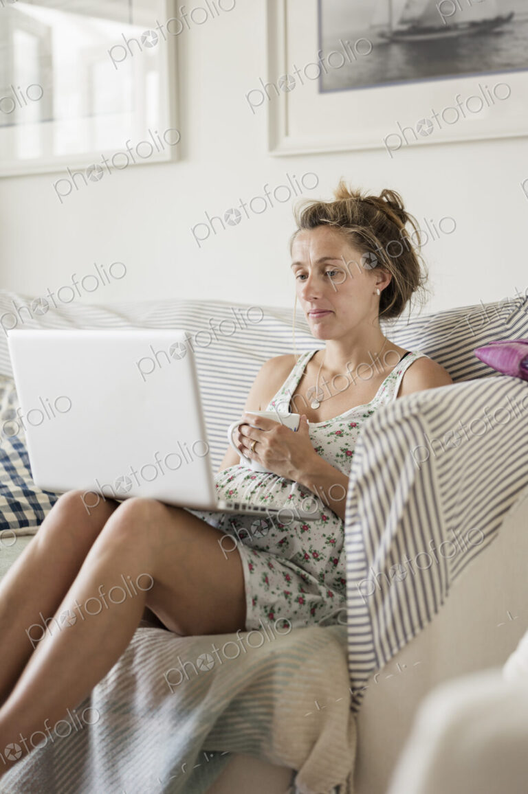 A pregnant woman seated on on a sofa with her feet up.
