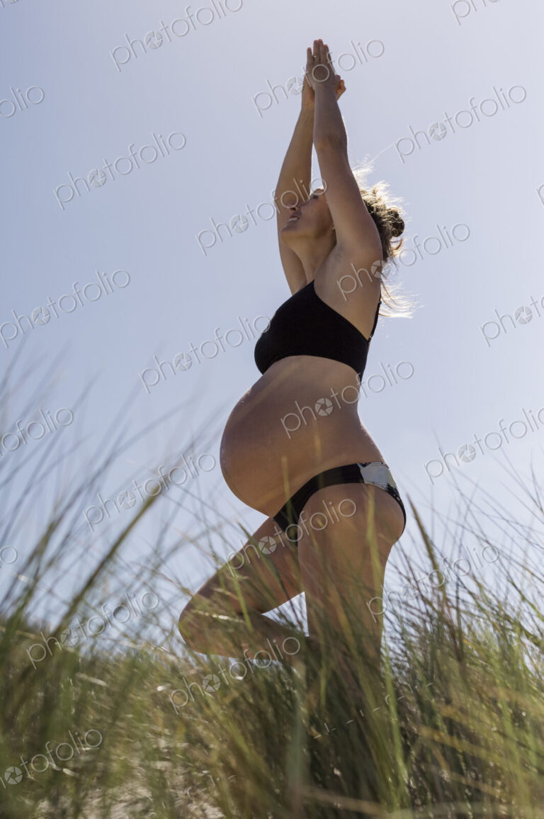 A pregnant woman standing in a yoga pose in the sunshine.