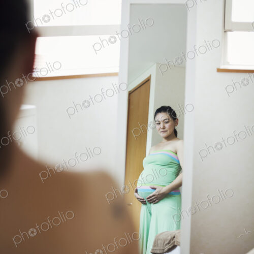 A pregnant woman standing in front of the mirror with her hands on her belly. A pregnant woman standing in front of the mirror with her hands on her belly.