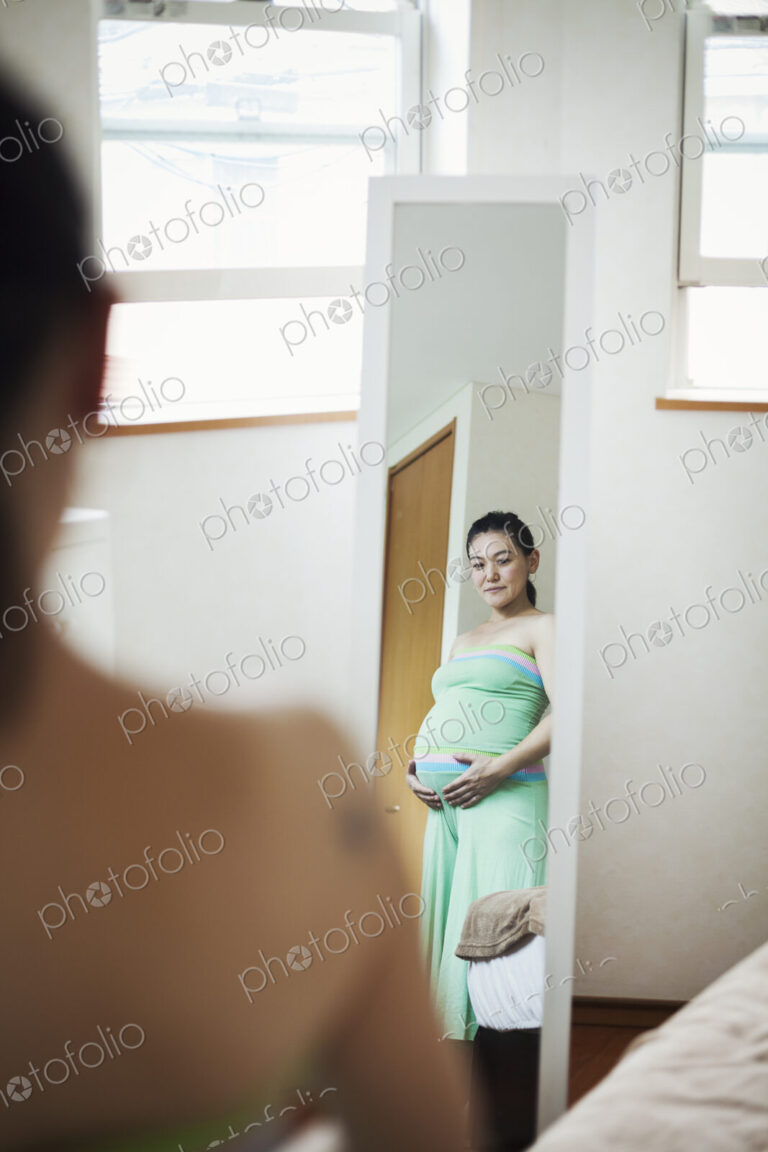 A pregnant woman standing in front of the mirror with her hands on her belly.