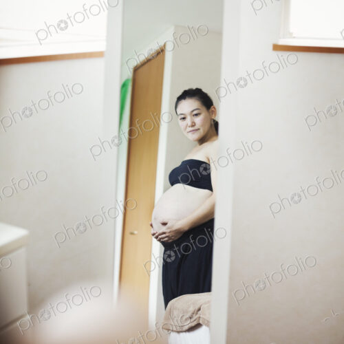 A pregnant woman standing in front of the mirror with her hands on her belly. A pregnant woman standing in front of the mirror with her hands on her belly.
