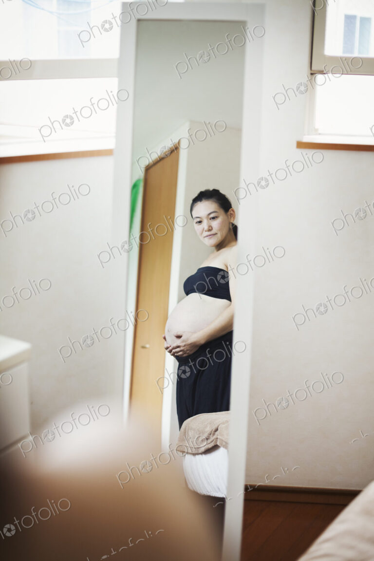 A pregnant woman standing in front of the mirror with her hands on her belly.