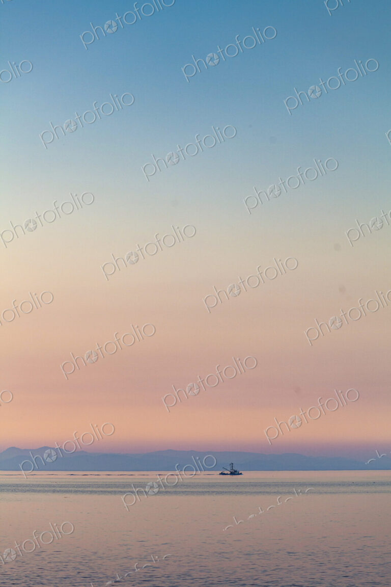 A purse seiner fishing vessel at dusk on the Strait of Juan de Fuca trailing a large net.