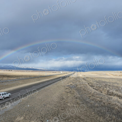 A rainbow in the sky above the highway I-90, a flat landscape and highway through… A rainbow in the sky above the highway I-90, a flat landscape and highway through…