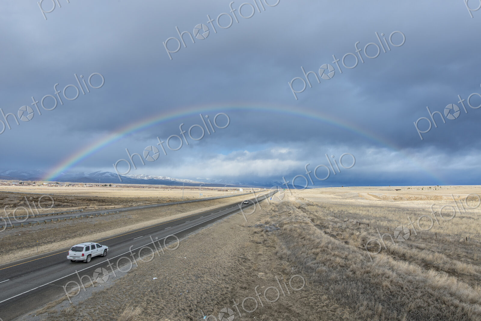 A rainbow in the sky above the highway I-90, a flat landscape and highway through…