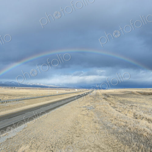 A rainbow in the sky above the highway I-90, a flat landscape and highway through… A rainbow in the sky above the highway I-90, a flat landscape and highway through…