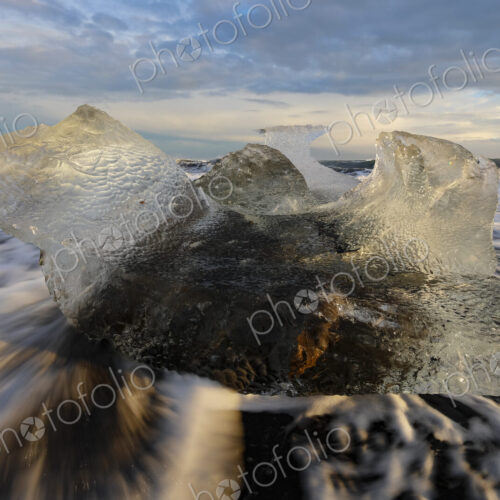 A receding wave and a chunk of calved Ice on the black sand beach at sunset A receding wave and a chunk of calved Ice on the black sand beach at sunset