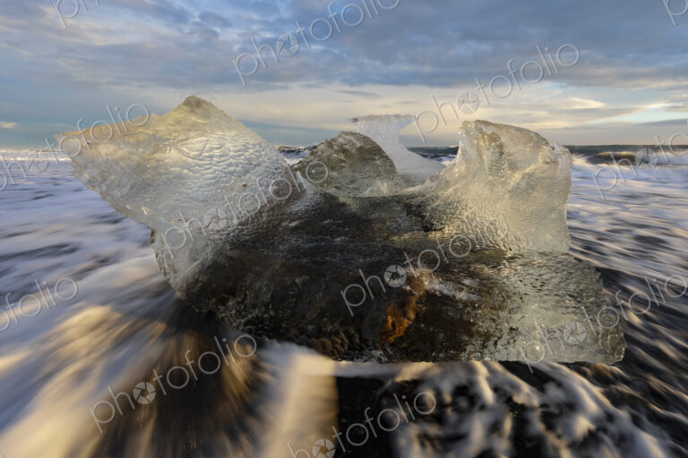 A receding wave and a chunk of calved Ice on the black sand beach at sunset