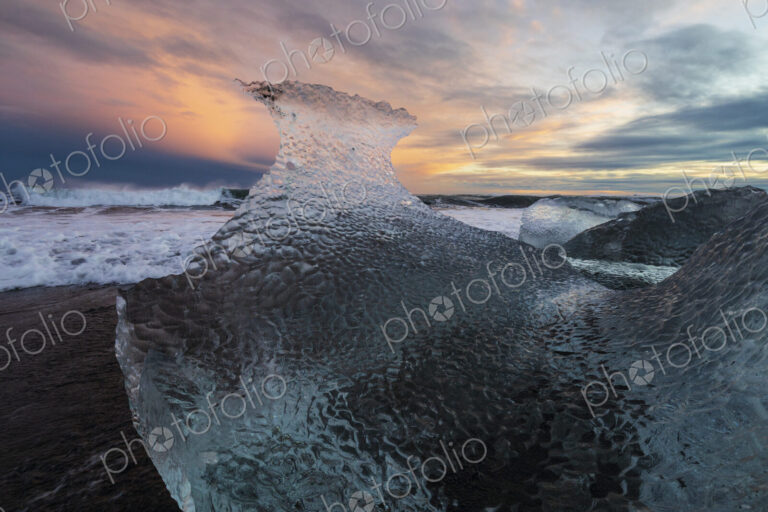 A receding wave and a chunk of calved Ice on the black sand beach at sunset