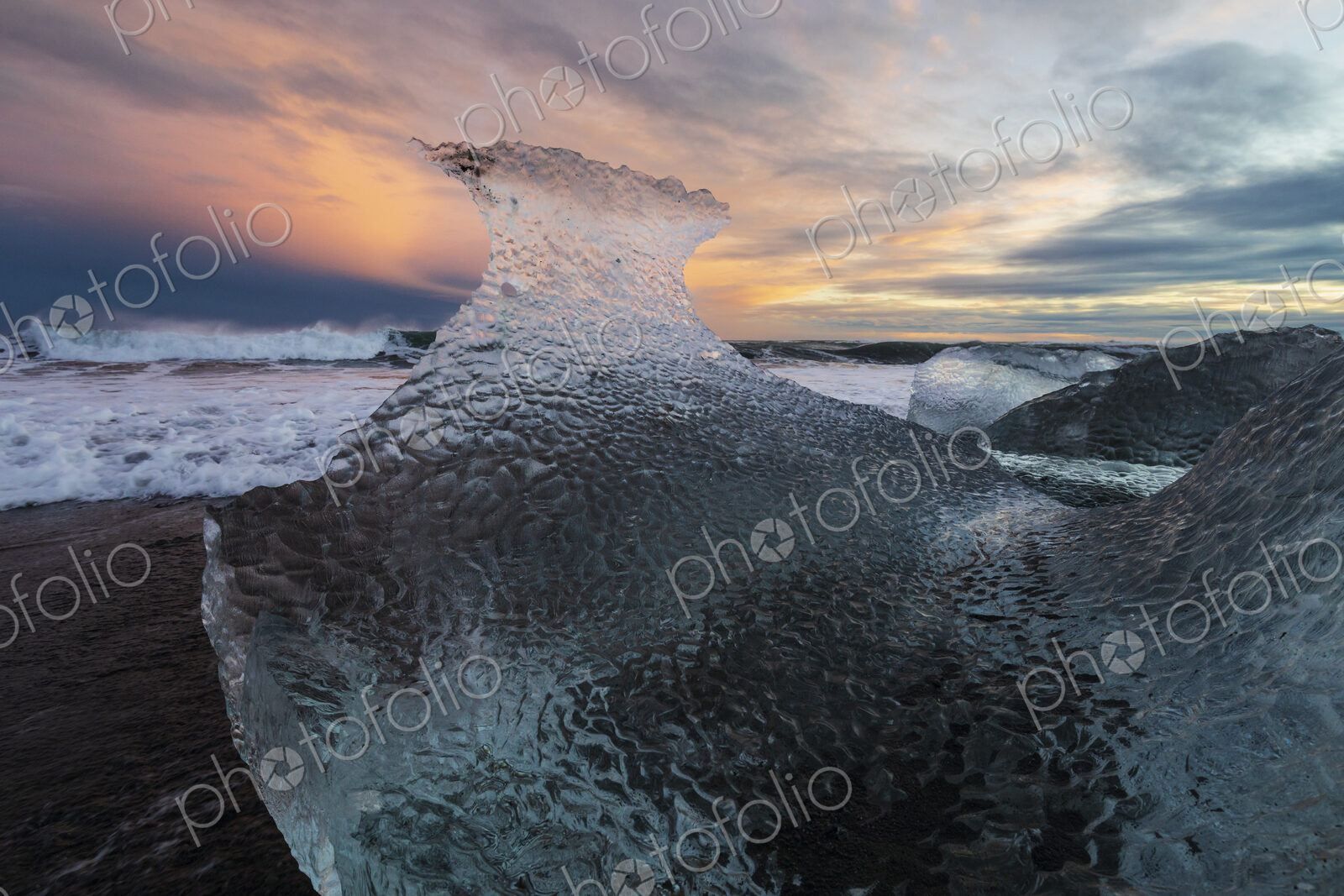 A receding wave and a chunk of calved Ice on the black sand beach at sunset