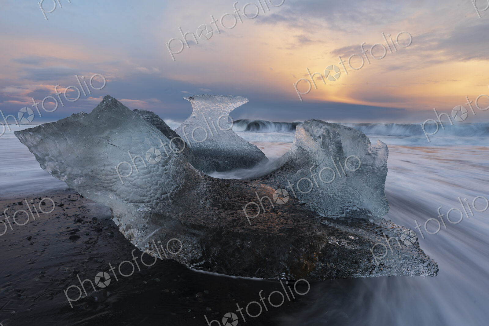 A receding wave and a chunk of calved Ice on the black sand beach at sunset