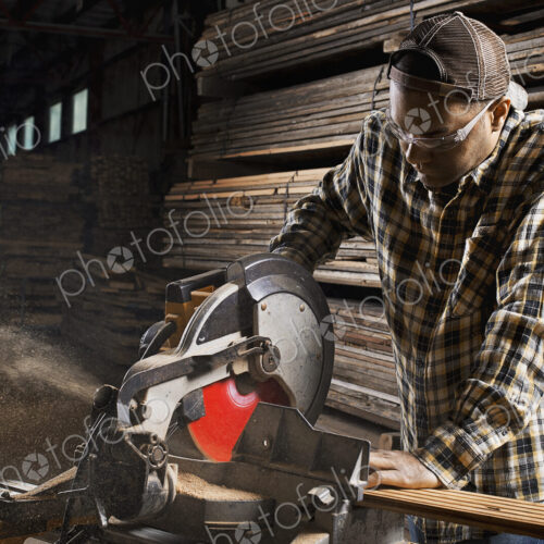A reclaimed lumber workshop. A man in protective eye goggles using a circular saw to…