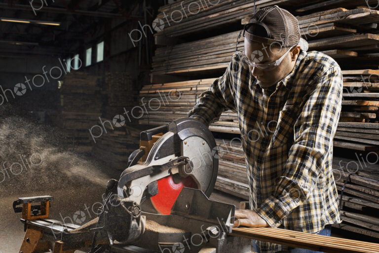 A reclaimed lumber workshop. A man in protective eye goggles using a circular saw to…