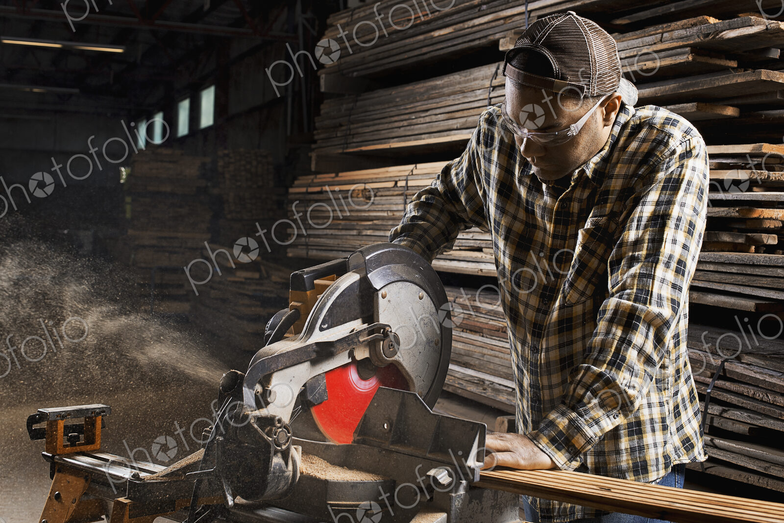 A reclaimed lumber workshop. A man in protective eye goggles using a circular saw to…