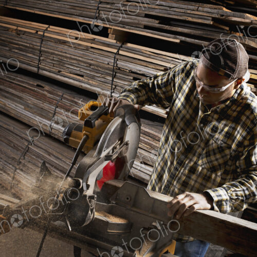 A reclaimed lumber workshop. A man in protective eye goggles using a circular saw to…